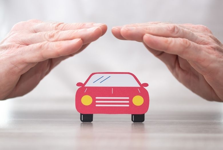 Um par de mãos protegendo um carro vermelho em miniatura