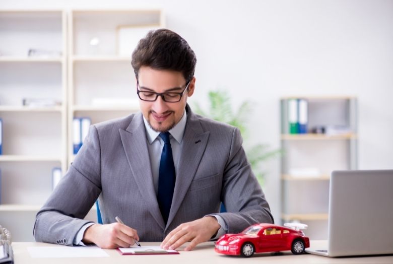 Homem escrevendo em um contrato e um carro em miniatura vermelho em cima da mesa